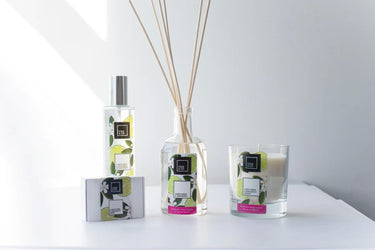 Reed diffusers, candles, and a glass of water on a table scented with Cole & Co Lime Flower & Bergamot Diffuser by Anna Davies.